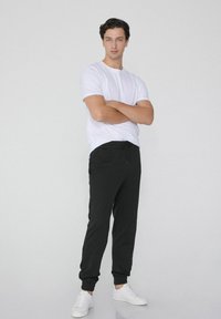 Zwarte sweats met elastische boorden en een trekkoord in de taille, gecombineerd met een plain wit t-shirt en witte sneakers. Eenvoudig, casual ontwerp.