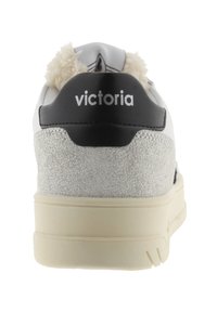 Sneaker bianca con suola crema, tacco testurizzato argentato, linguetta nera sul tallone etichettata "victoria" e rivestimento in pile beige visibile nella parte superiore.