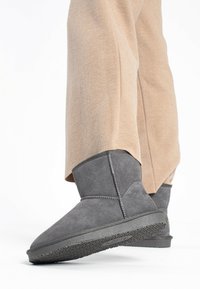 Grå mocka ankelboots med en platt gummisula, med en rund tå och sydda detaljer, i kombination med ljusbeige byxor.