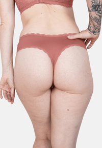Rose-colored lace-trimmed underwear, featuring a ribbed texture and a cheeky cut, with a scalloped edge along the waistband.