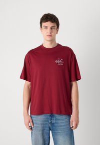 Bordo pārmērīgs t-krekls, izgatavots no kokvilnas, ar mazu "Calvin Klein" logotipu baltā krāsā uz krūtīm, īsām piedurknēm un apaļu kakla izgriezumu.