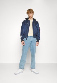 Mornarska pilotska jakna sa patentnim zatvaračem, rebrastim manžetama i crnom kapuljačom. Uparena sa svijetloplavim trapericama i bijelim tenisicama.