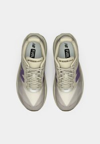 Beige jooksujalad lilla aktsentidega. Kerge võrkkangas ülemine osa, pehmendusega vaheosa, tekstureeritud varbakiil ja lapikud paelad. Suure nähtavusega bränding.