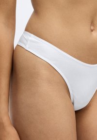 Witte katoenen stringonderbroek met een gladde textuur, minimalistisch ontwerp en een lage tailleband. Geen patronen of accenten zichtbaar.