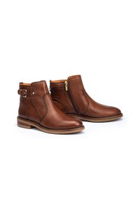 Botas de cuero marrón hasta el tobillo con cierre de cremallera, hebilla decorativa, punta redonda y tacón bajo apilado. Textura suave y forro naranja en contraste.