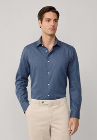 Blauw overhemd met lange mouwen en een button-down kraag, gemaakt van textuurstof, met witte knopen en gecombineerd met lichtbeige broeken.