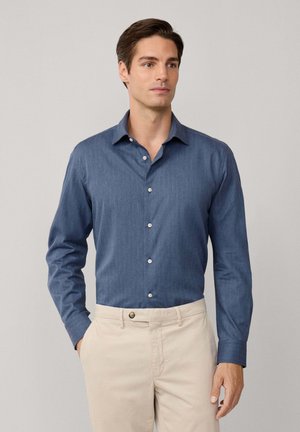 Camisa de manga larga azul con cuello tipo button-down, hecha de un tejido texturizado, con botones blancos y combinada con pantalones beige claros.