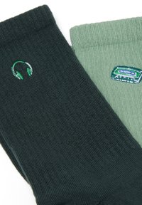 Dunkelgrüne und hellgrüne Socken mit bestickten Designs: Kopfhörer auf der dunklen Socke und ein Kassettenband auf der hellen Socke. Weiches Material.