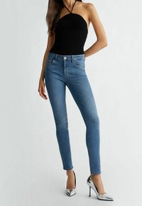 Modré džíny s úzkým střihem a bledými místy, doplněné o přiléhavý černý žebrovaný top a stříbrné vysoké podpatky.