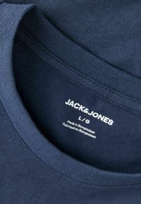 Gros plan du col d'un t-shirt bleu marine Jack & Jones montrant la taille L/G et une étiquette « Fabriqué au Bangladesh » à l'intérieur.