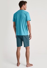 Turquoise T-shirt met korte mouwen en marineblauwe gestippelde shorts. T-shirt heeft een ronde hals; shorts hebben een geometrisch patroon en zijn boven de knie.