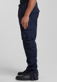 Mörkblå cargobyxor i bomullsblandat tyg med flera fickor, avslappnad passform och förstärkta knän. Bärs med svarta höga sneakers.