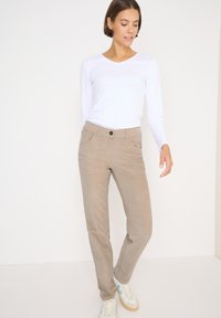 Béžové kordové kalhoty se rovnými nohavicemi, s předními kapsami, zapínáním na knoflík a měkkou strukturou, v kombinaci s bílým tričkem s dlouhým rukávem.