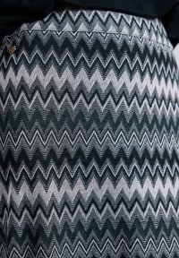 Tissu d'une jupe à motif zigzag noir et blanc, montrant une texture détaillée du tricot et un petit bouton métallique rond près de la taille.