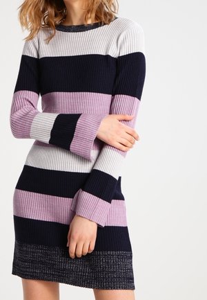 Femme portant une robe tricotée à côtes à manches longues avec de larges rayures horizontales blanches, marine, rose et noires.