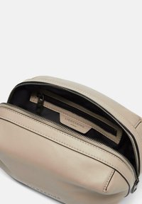 Beżowa skórzana kosmetyczka z zamkiem błyskawicznym, posiadająca czarne wnętrze i małą kieszonkę na zamek, oznaczoną napisem "LIEBESKIND" wewnątrz.