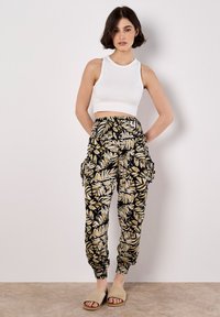 Top court côtelé blanc associé à un pantalon cargo noir avec un motif de feuilles jaunes, des poignets élastiques et des poches latérales. Sandales beiges à enfiler.