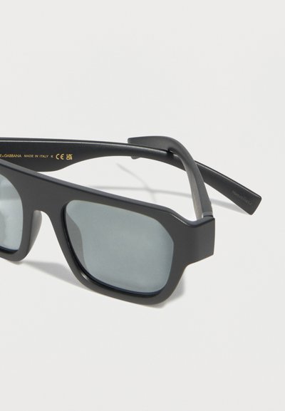 Μαύρα ματ ορθογώνια γυαλιά ηλίου με σκουρόχρωμους φακούς και ελαφρώς χοντρά πλαίσια σε λευκό φόντο.