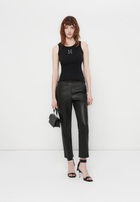 Haut sans manches noir au design ajusté avec des détails brodés, associé à un pantalon en cuir noir taille haute et des talons aiguilles noirs à lanières.