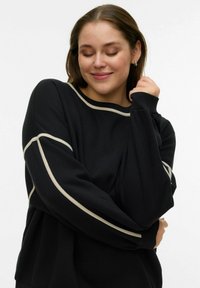 Czarna bluza z kremowymi akcentami wzdłuż dekoltu i rękawów. Ma luźny krój z ściągaczami na mankietach i miękką fakturę.