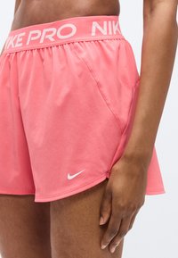 Pink Nike Pro-shorts med elastisk taljebånd med teksten "NIKE PRO." Inkluderer en lille hvid Nike swoosh-logo på siden.