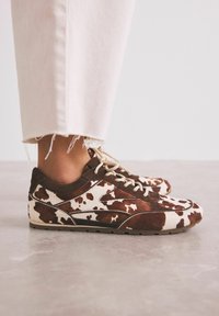 Ruskean ja valkoisen lehmäkuosiset tennarit, joissa on nahan tuntu, pyöreä kärki ja beige kengännauhat. Varustettu matalaprofiilisella kumipohjalla ja yksityiskohtaisella ompelulla.