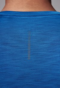 Primo piano della parte superiore della schiena di una persona che indossa una camicia in tessuto blu testurizzato con una striscia riflettente verticale al centro.