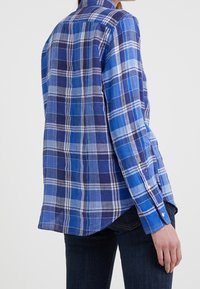 Blå och marinhjärtad skjorta gjord av lättviktsmaterial. Har knäppte manschetter och en böjd fåll, med en klassisk krage och strukturerad design.