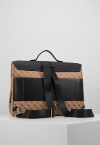 Serviette marron à motifs avec des accents en cuir noir, poignée supérieure et bandoulière noire réglable reposant sur une surface blanche.