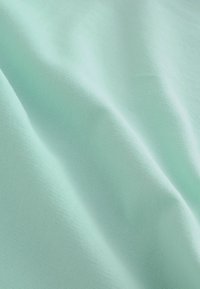 Tissu doux de couleur turquoise claire avec des plis légers et une texture lisse, éclairé uniformément sans motifs ni objets visibles.