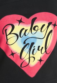 Černá látka se srdcovým grafickým vzorem v růžové, žluté a modré barvě, s textem "Baby Girl" napsaným tučným černým písmem a akcenty hvězd.