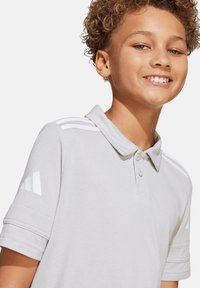 Graues Poloshirt mit Kragen, kurzen Ärmeln und drei weißen Streifen auf den Schultern. Mit Adidas-Logo auf dem linken Arm.