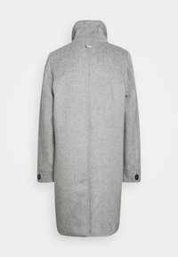 Manteau en laine grise avec un col montant, une fente arrière et des poignets boutonnés. Présente un design minimaliste avec une texture chevron subtile.