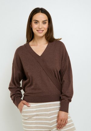 Maglione marrone a portafoglio con scollatura a V, vestibilità ampia e dettagli a coste sui polsini, abbinato a pantaloni beige a righe. Tessuto morbido e texture.