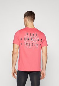Triko Nike Running Division v růžové bavlně s výrazným černým grafickým nápisem a vzorem leopardího tisku na zadní straně. Krátké rukávy.