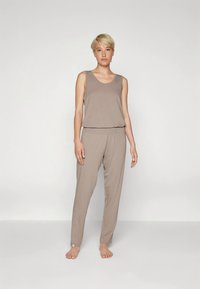 Camisola de alças castanha clara e calças a condizer feitas de tecido macio. A camisola tem decote em U; as calças possuem cintura elástica e corte relaxado.