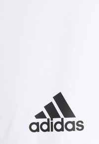 Valge spordipusa sujuva tekstuuriga, millel on silmapaistev must Adidas'i logo ja kolm diagonaalset triipu vasakus alumises nurgas.