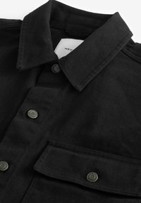 Zwart corduroy overhemd met een puntige kraag, drukknopen en borstzakken met een gestructureerd stoffenpatroon. Label zichtbaar aan de binnenkant van de kraag.