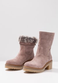 Pink suede ankle boots with a gray faux fur cuff, featuring a thick platform sole and rounded toe. Detailed stitching on the sides.