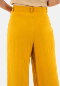 Pantaloni larghi gialli realizzati in un tessuto testurizzato, con una cintura liscia, tasca posteriore e una vestibilità comoda.