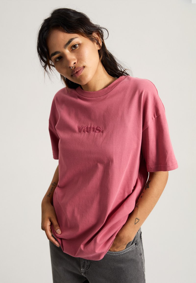 Camiseta de algodón rosa con mangas cortas, escote redondo y logo bordado en el pecho. Textura suave y corte holgado.