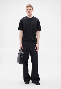 Fekete pamutpóló kis logóval, sötétkék farmer bő szárú nadrággal párosítva. Fekete bőr táskát tart kézi fogantyúval.