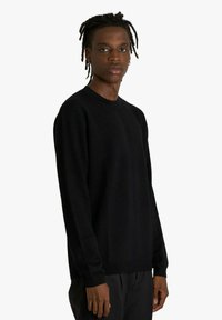 Maglione nero a maglia con maniche lunghe, scollo rotondo e vestibilità morbida. Texture liscia, design minimale, senza motivi o accenti visibili.