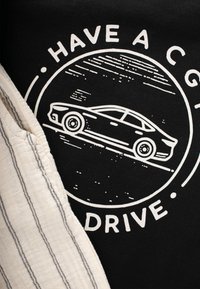 Camiseta negra con un gráfico blanco de un coche y el texto "TEN UN BUEN VIAJE," junto a una tela de rayas color crema.