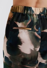 Kevytkankaista, kukkakuosilla varustetut housut, joissa on piilotettu tasku, joustava vyötärö ja väreinä musta, vihreä ja kerma.