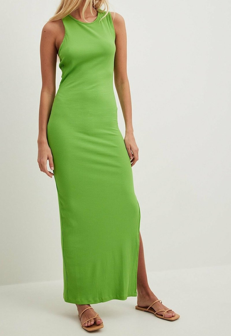 Abito lungo senza maniche verde a coste con uno spacco laterale e scollatura rotonda, realizzato in materiale morbido ed elasticizzato. Indossato con semplici sandali beige.