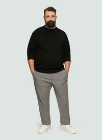 Czarny sweter z okrągłym dekoldem, szare spodnie w wzory i białe sneakersy. Stylizacja jest casualowa, z luźnym krojem i minimalnymi akcentami.