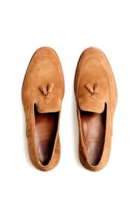 Mocassini in camoscio marrone con una texture morbida, dettaglio con nappe sul davanti, punta tonda e soletta in pelle. Suola piatta, senza marchi visibili.