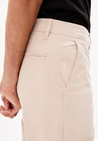 Světle růžové chinos kalhoty s úzkým střihem, kapsami po stranách a texturovanou látkou. Jemný detail s logem u kapsy.