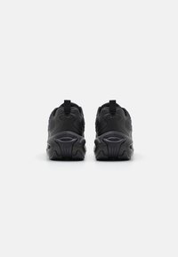 Chaussures de sport noires avec des surfaces texturées, des talons arrondis et des semelles en caoutchouc proéminentes. Dotées de languettes et d'un design lisse et futuriste.